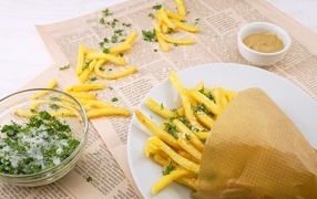 French fries on the table with newspaper, salt and herbs