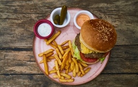 Hamburger on a plate with french fries, cucumbers and sauce