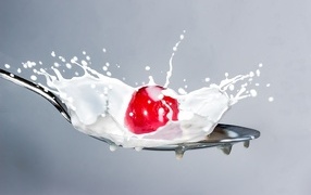 Red cherries in a spoon with milk on a gray background