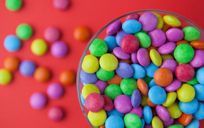Разноцветные конфеты в стакане на красном столе