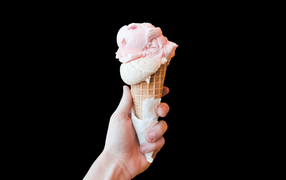 Розовое мороженое в рожке в руке на черном фоне