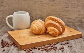 Two croissants on a board with coffee beans