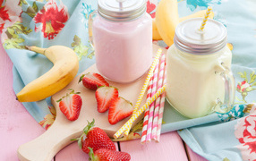 Two jars of smoothies on the table with banana and strawberries