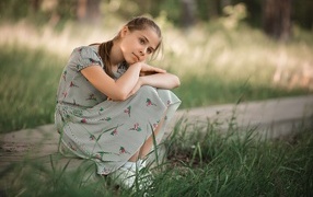 A girl in a dress sits near the green grass