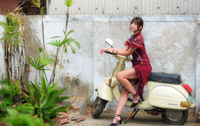 Asian girl sitting on a scooter against the wall