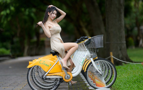Азиатка в платье сидит на велосипеде