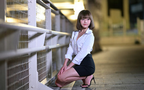Азиатка в белой блузке и черной юбке сидит на корточках