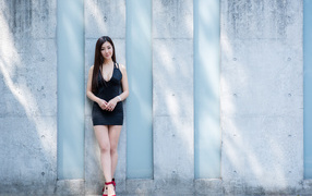Beautiful Asian woman in a short dress stands against the wall