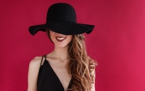 Черная шляпа на лице у девушки на розовом фоне