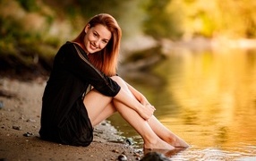 Smiling girl in a black dress sits by the water