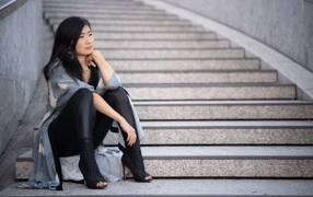 Задумчивая девушка азиатка сидит на ступеньках