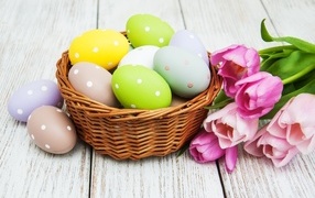 Корзина разноцветных яиц с тюльпанами на столе на Пасху