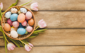 Basket with colored eggs and pink tulips on a wooden table for Easter