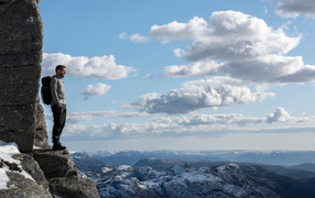 A man stands on the edge of a cliff against the sky