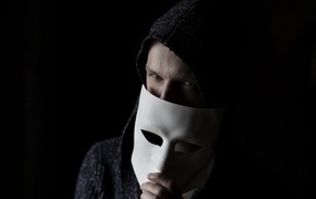 A man with a white mask in his hand on a black background