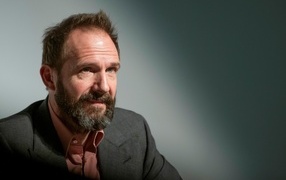 Actor Ralph Fiennes with a beard on a gray background