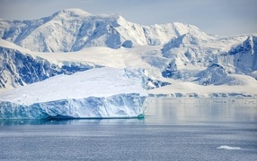 Large iceberg off the coast with snow-capped mountains
