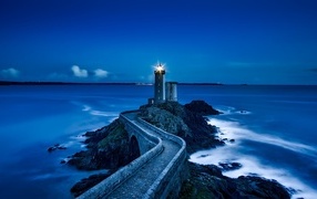 Lighted lighthouse on the seashore at night
