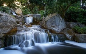 The waterfall flows down over large cold stones in the forest