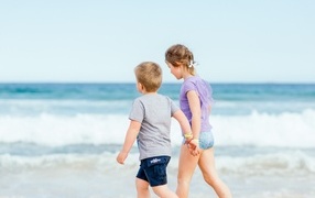 A boy and a girl walk along the sand by the sea