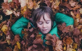A little girl with her eyes closed lies in dry leaves