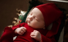Маленький ребенок спит в красном костюме