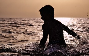 Маленький мальчик купается в воде летом