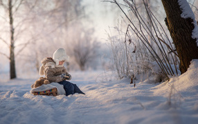 Маленький ребенок на санках в зимнем лесу 