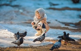 Маленькая девочка кормит голубей зимой