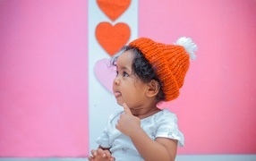 Little girl in a knitted hat on a pink background