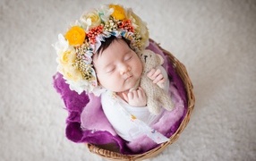 Newborn baby girl with a wreath on her head sleeps in a basket