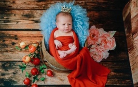 Новорожденный ребенок в красном покрывале с короной на голове 