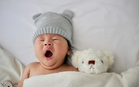 Newborn baby with a toy yawns in bed
