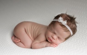 Новорожденная малышка с белой лентой на голове
