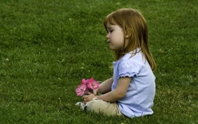 Sad little girl sitting on the green grass