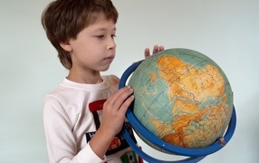 Школьник изучает глобус на сером фоне