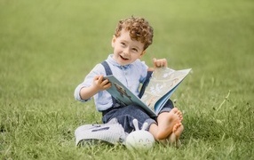 Smiling boy with a book sitting on the grass