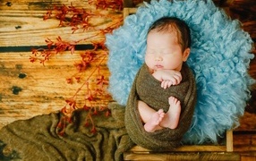Крошечный новорожденный ребенок на голубой меховой подушке