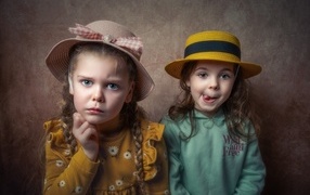 Two little girls in hats against a brown wall