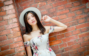 Asian woman in a white hat stands against a brick wall