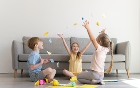 Дети играют на полу  в комнате с серым диваном