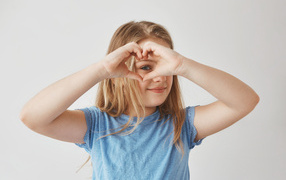 Girl makes a heart with her hands on a gray background