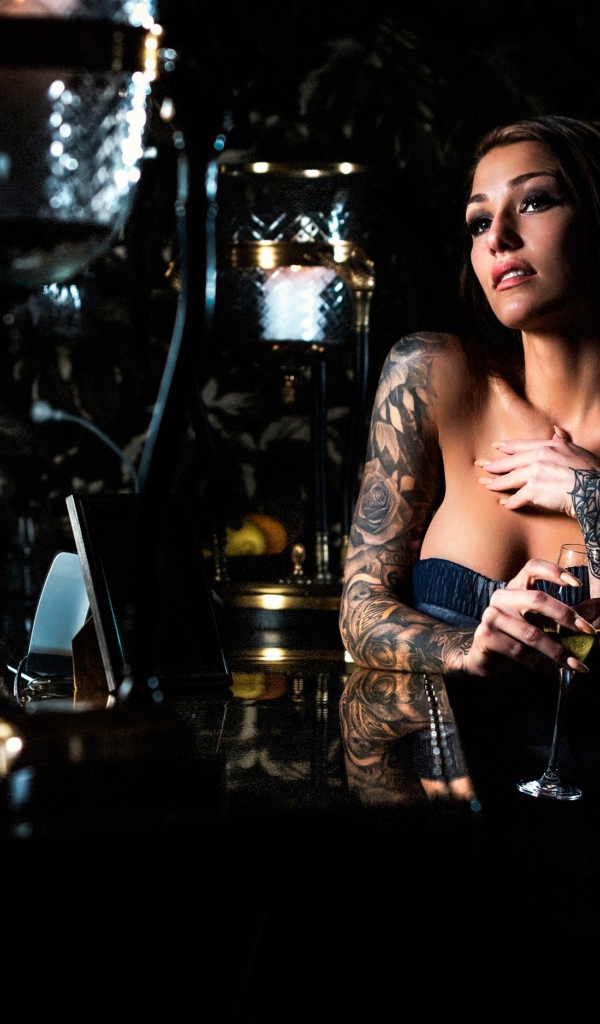 Татуированная девушка пьет вино в баре
