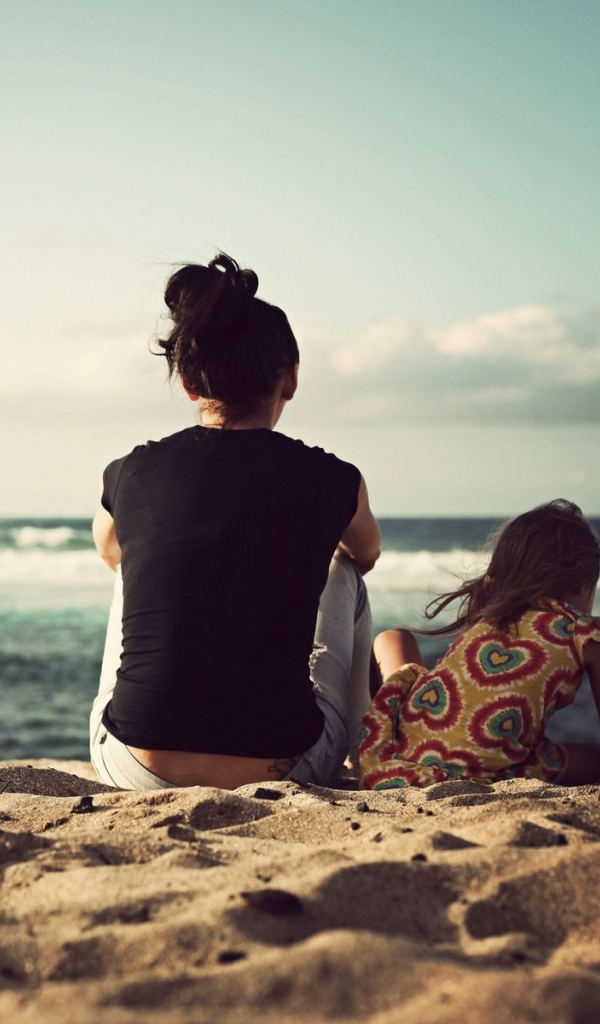 Женщина с дочкой сидят на песке на берегу моря