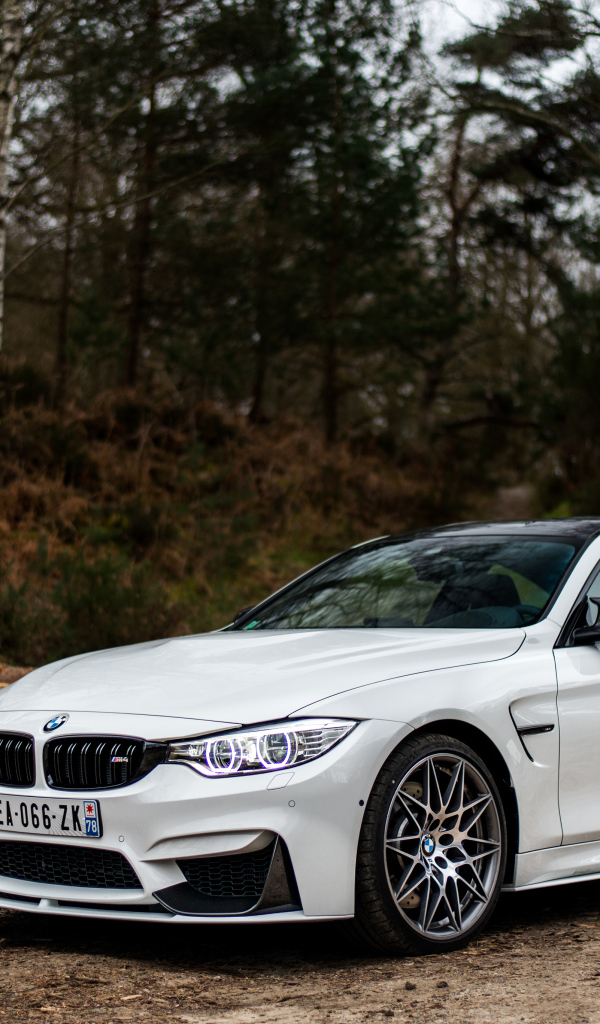 Белый стильный автомобиль BMW M4 на фоне деревьев