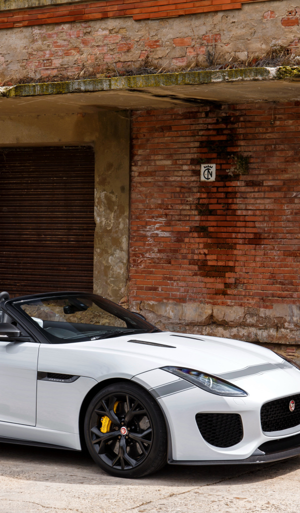 Белый автомобиль Jaguar F-Type у красной кирпичной стены