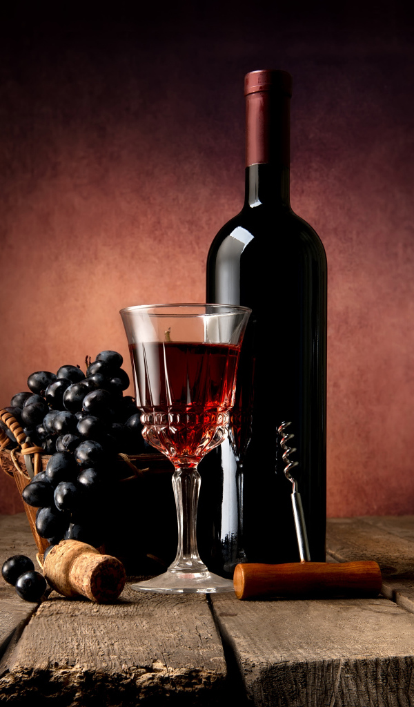 Бутылка красного вина на столе с бокалом и синим виноградом
