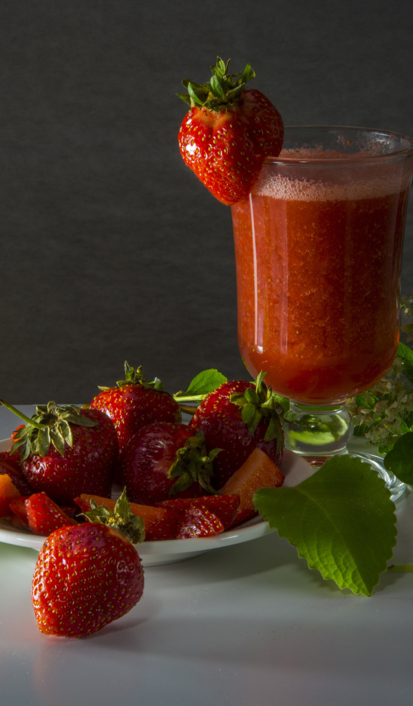 A glass of strawberry juice and fresh strawberries on a table