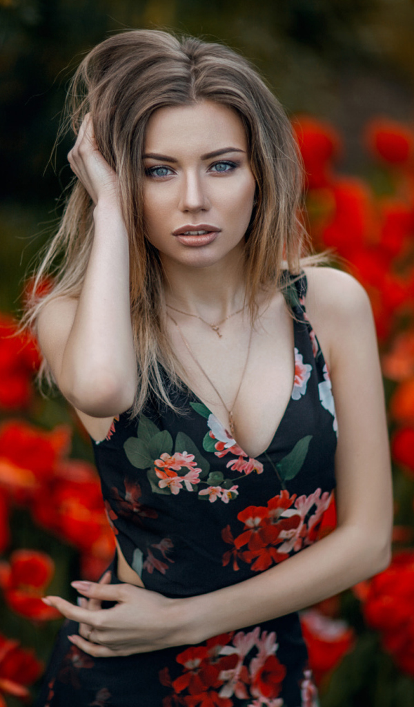 Красивая молодая девушка позирует на фоне красных тюльпанов