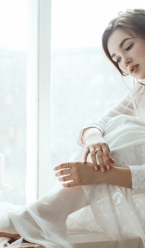 Молодая грустная девушка в белом платье у окна